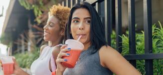 Two women drinking smoothies outside.
