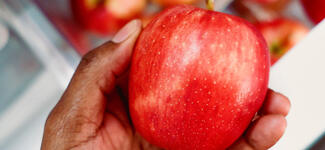 A hand holding a red apple in kitchen.