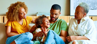 A family sits on the couch talking happily.