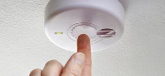 Closeup of a hand testing a fire alarm.